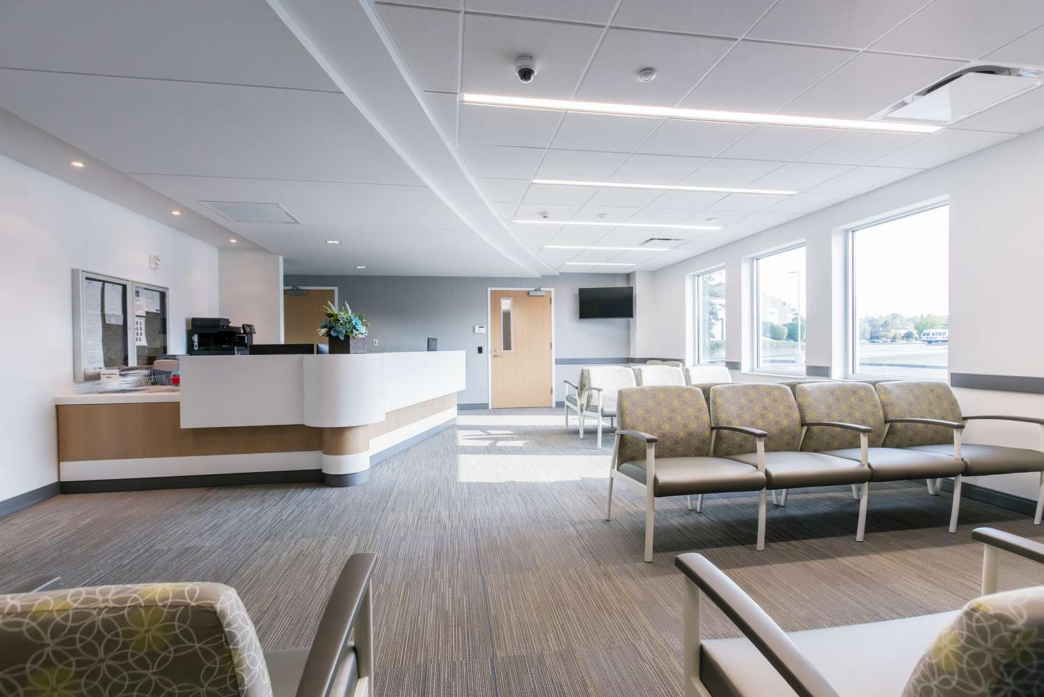 A calm urgent care waiting room with a front desk staff member assisting a patient