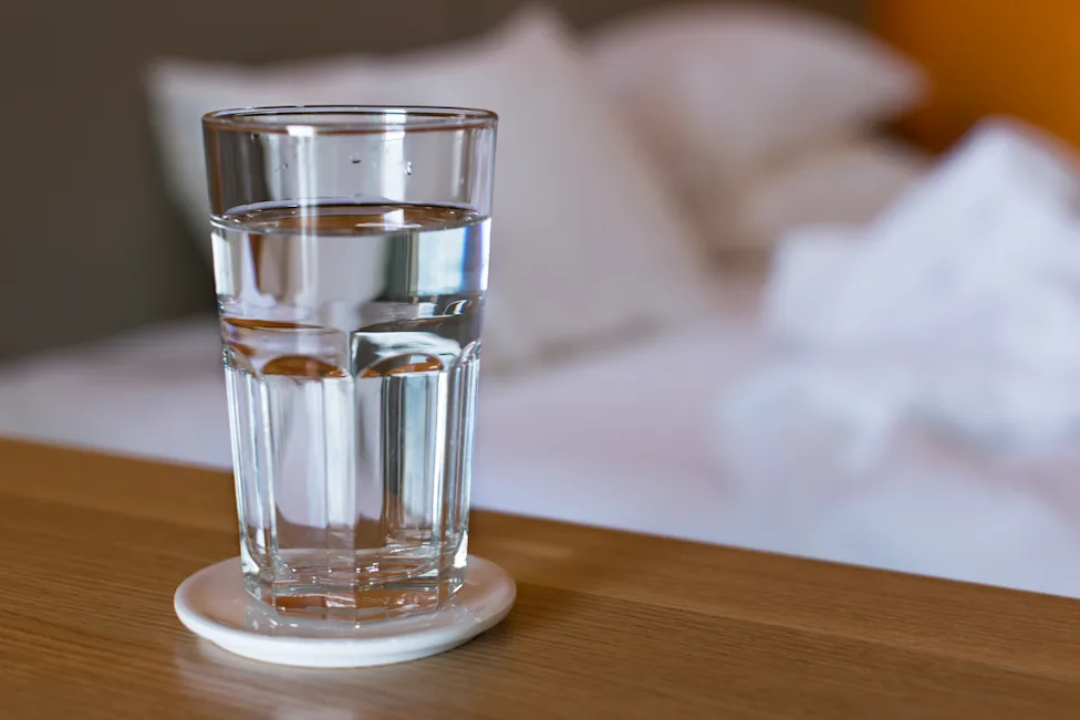 A clear glass of water beside a reusable water bottle in natural daylight