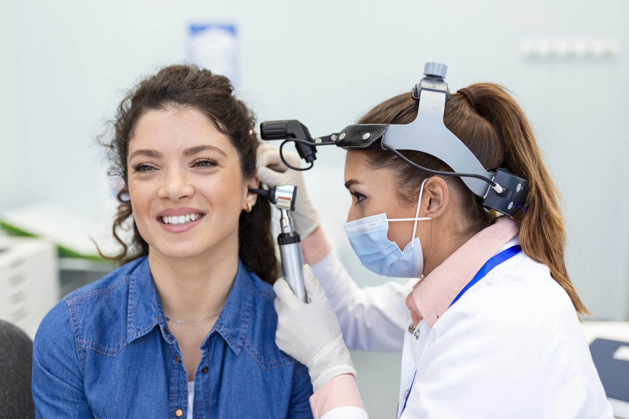 A clinician in a medical exam room examining a patient’s ear with an otoscope during an ear checkup