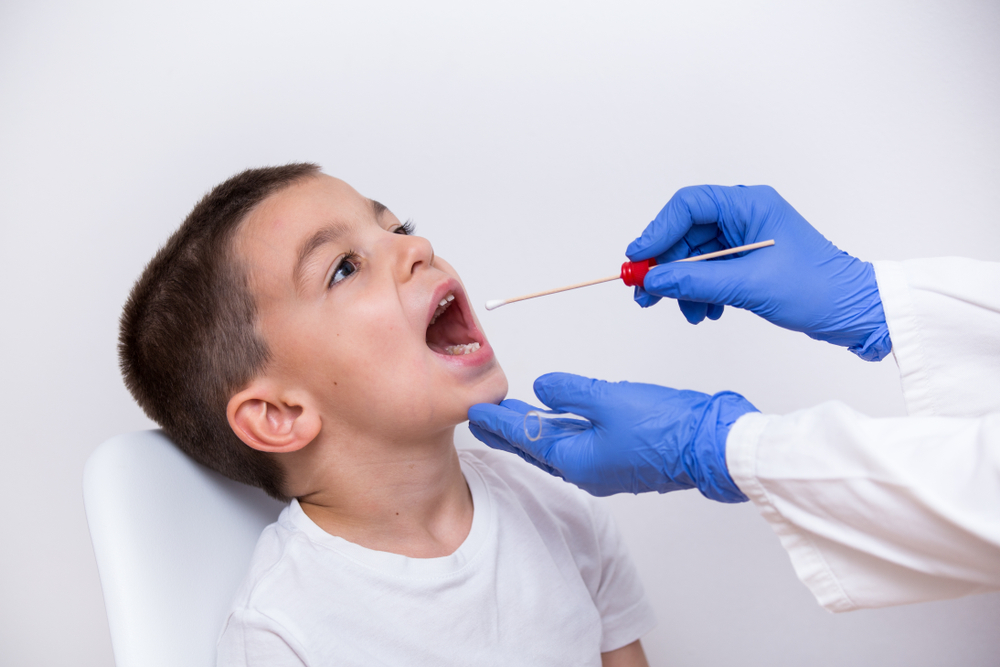 A clinician in a medical exam room gently swabbing the back of an adult patient’s throat with a sterile cotton swab, preparing a sample for rapid testing