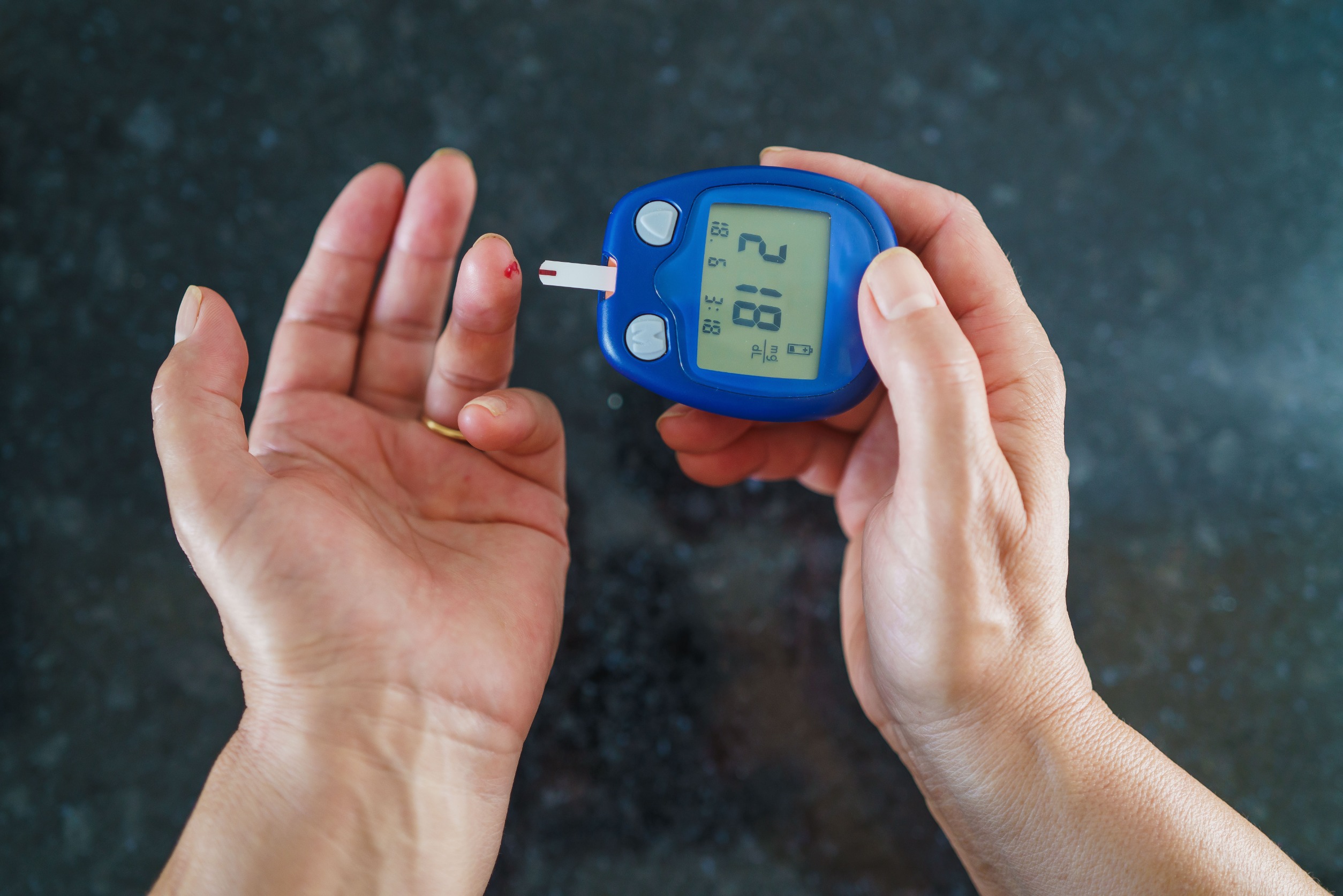 A close-up of a person performing a fingerstick blood sugar check at home with a glucometer on a kitchen table