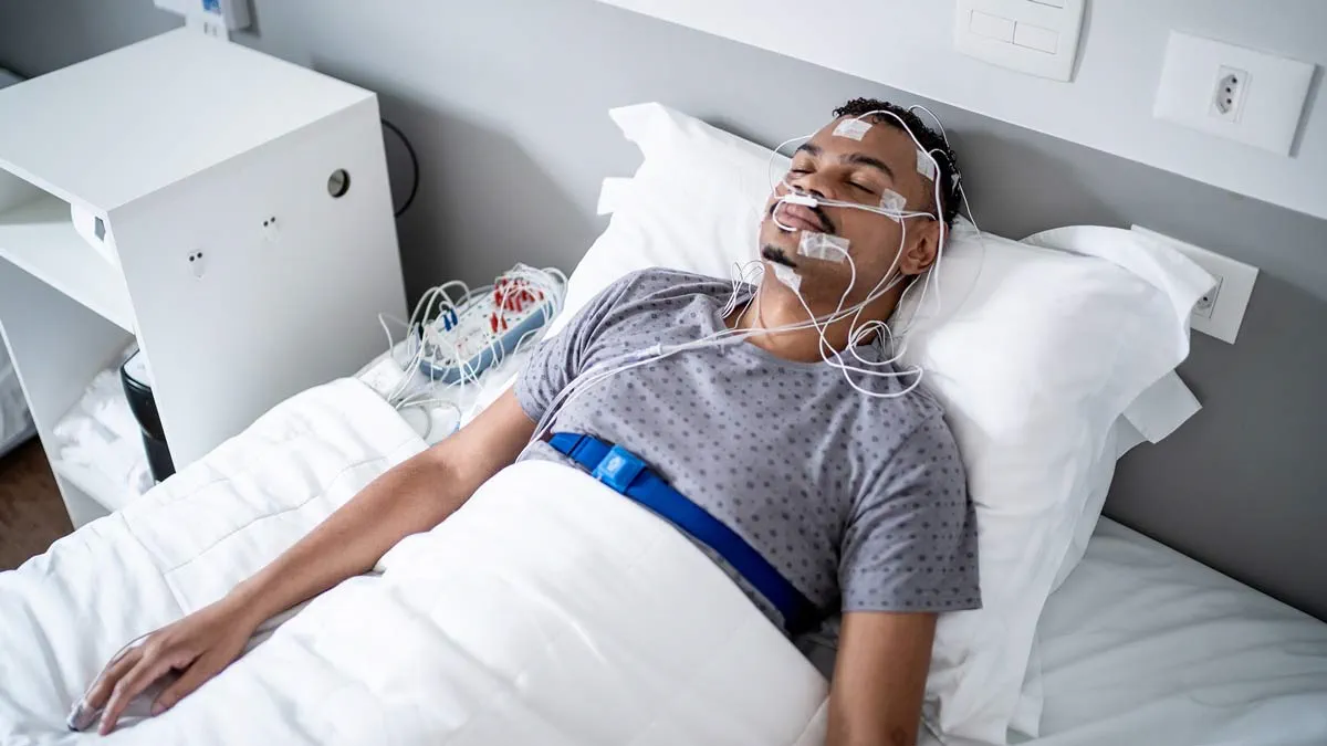 A patient lying in bed during an overnight sleep study with monitoring sensors attached, in a calm clinical sleep lab room