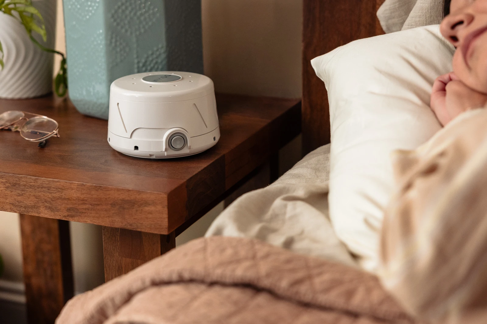 A person asleep in a dim bedroom with a small white noise machine on a bedside table