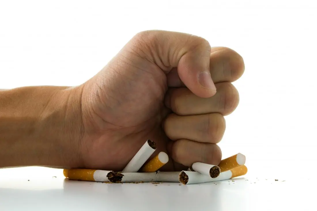 A person holding a crumpled cigarette pack and lighter over a kitchen counter, suggesting a decision to quit smoking