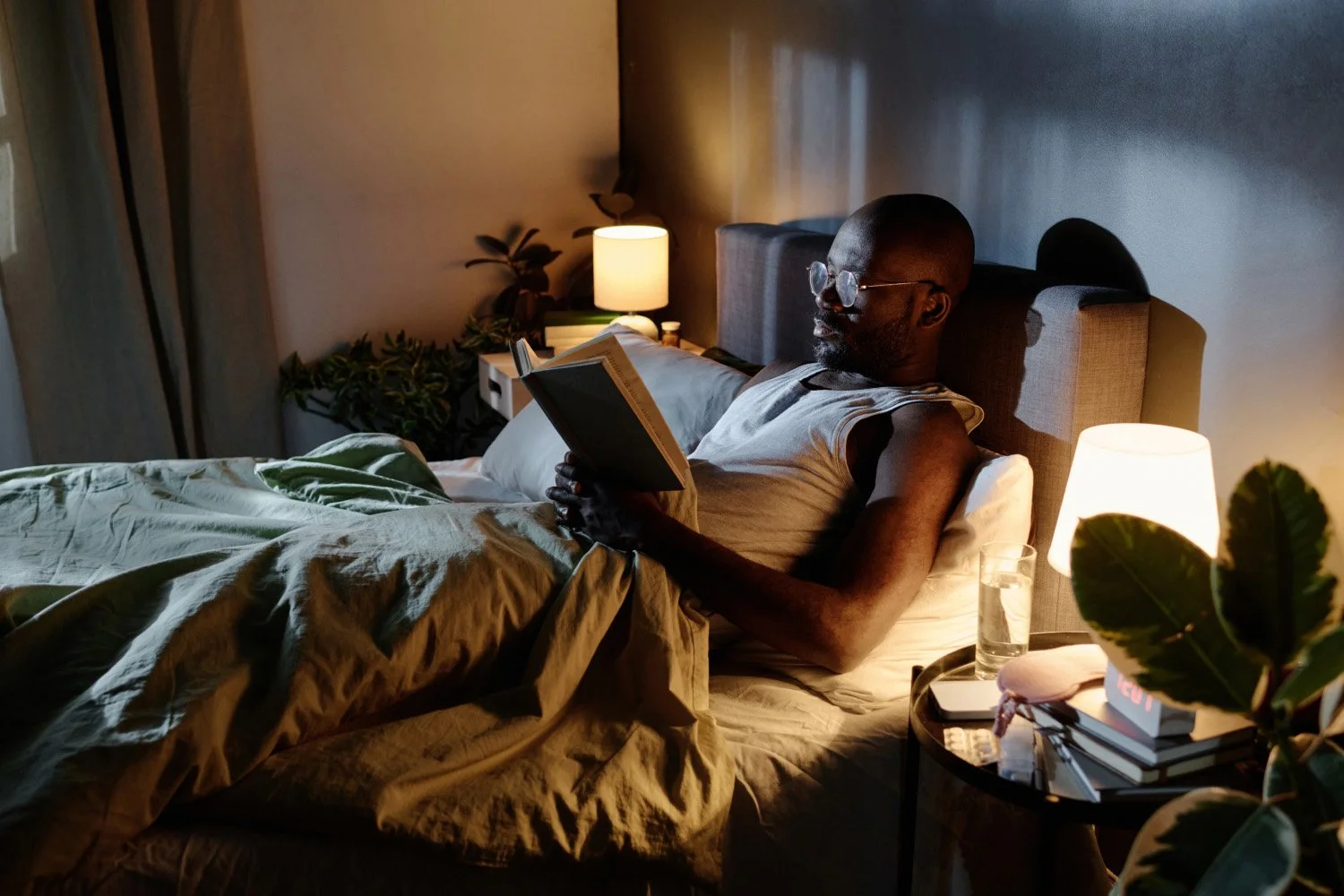 A person sitting up in bed reading a book under a soft bedside lamp with a calm evening atmosphere