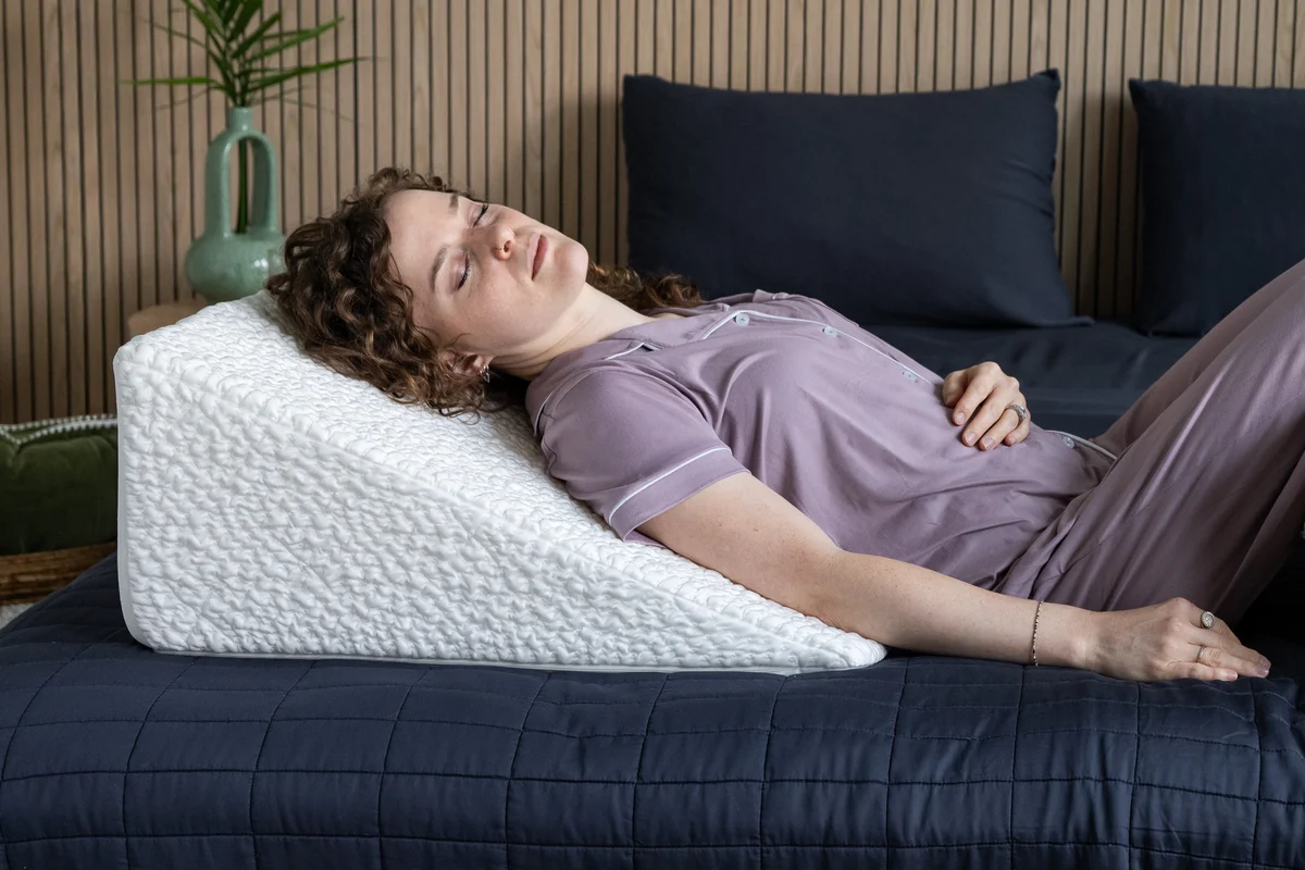 A person sleeping on their side with the head and upper torso elevated on a wedge pillow in a softly lit bedroom