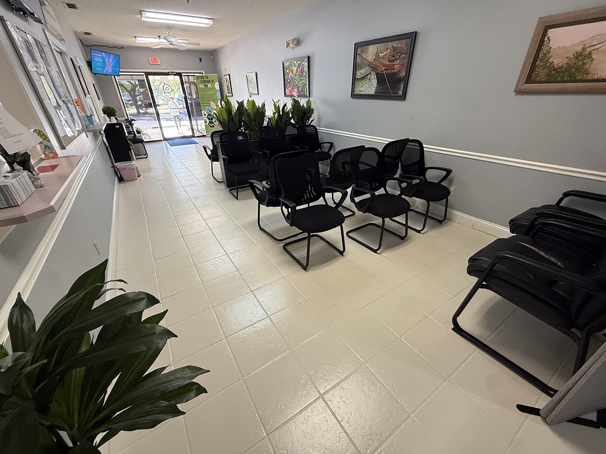 Adults seated in a bright urgent care waiting room, one person holding a tissue and a cup of water while waiting to be called