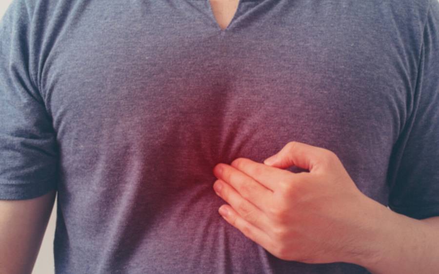 An adult sitting upright on a couch at night holding their chest with a mildly uncomfortable expression, suggesting heartburn symptoms in a real home setting