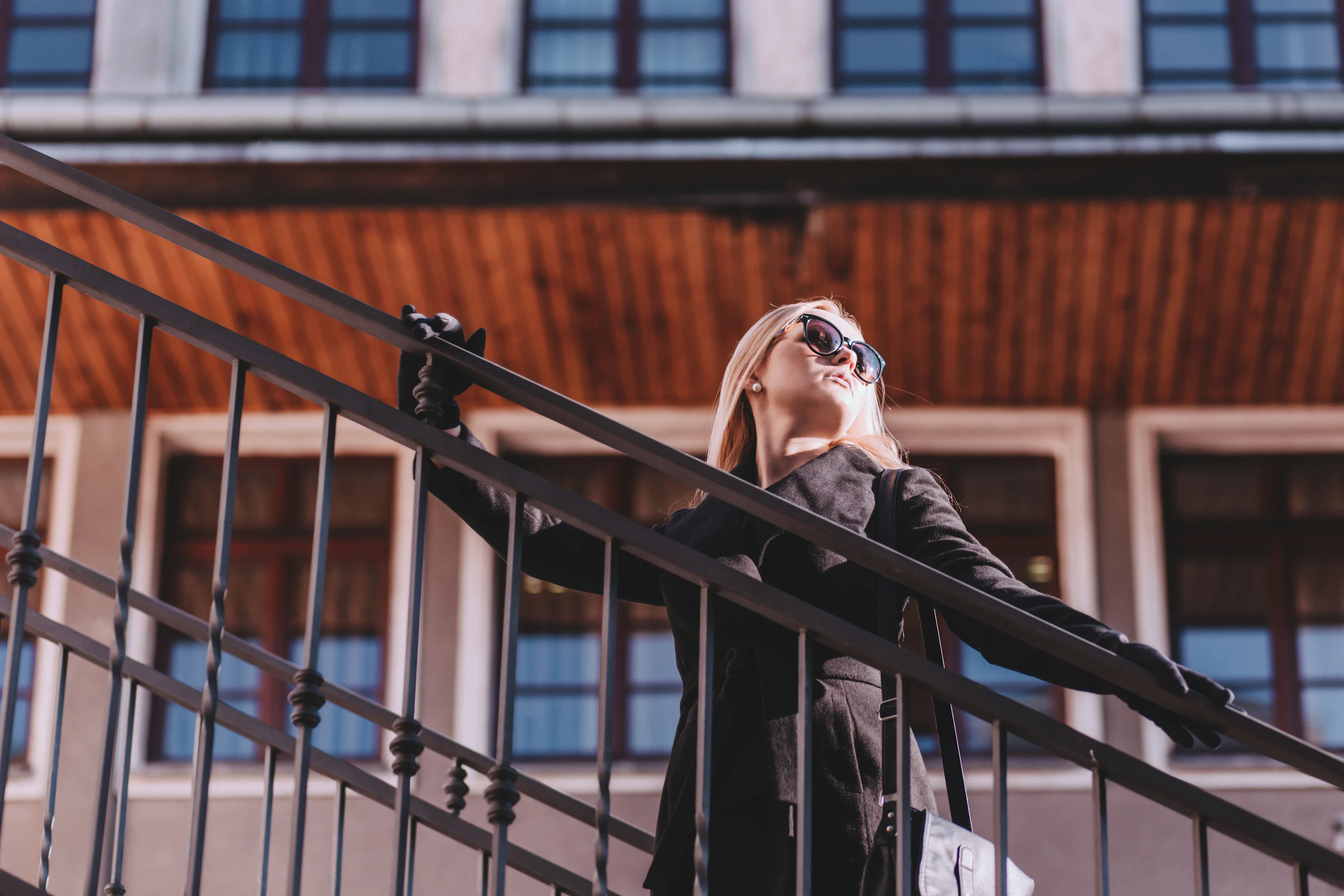 An adult woman pausing on an indoor staircase while holding the railing, eyes closed briefly as if feeling unsteady